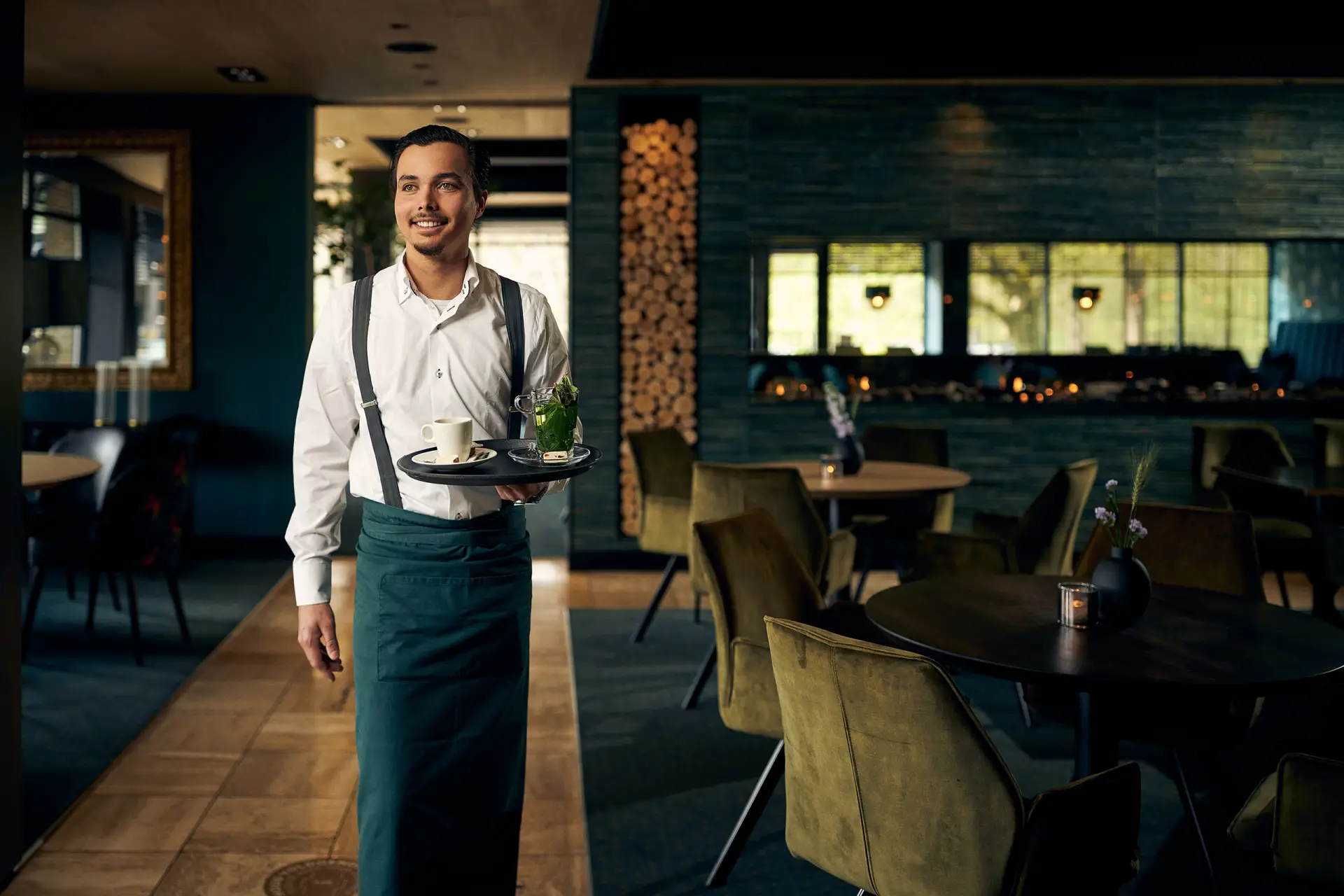 Lopende ober met een dienblad in een restaurant met groen/blauwe tinten