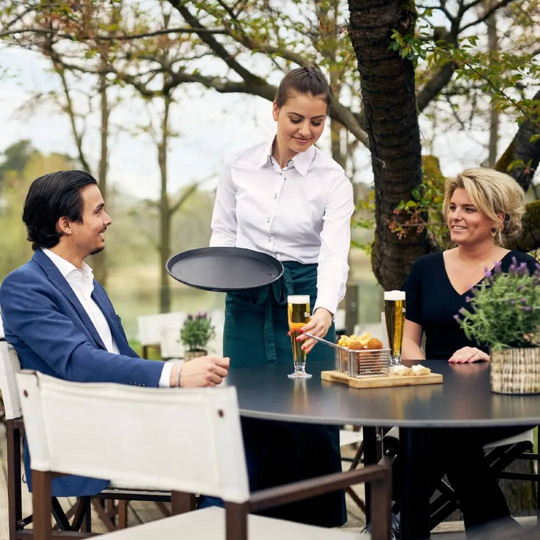 Medewerker bediening serveert bier aan gasten op terras