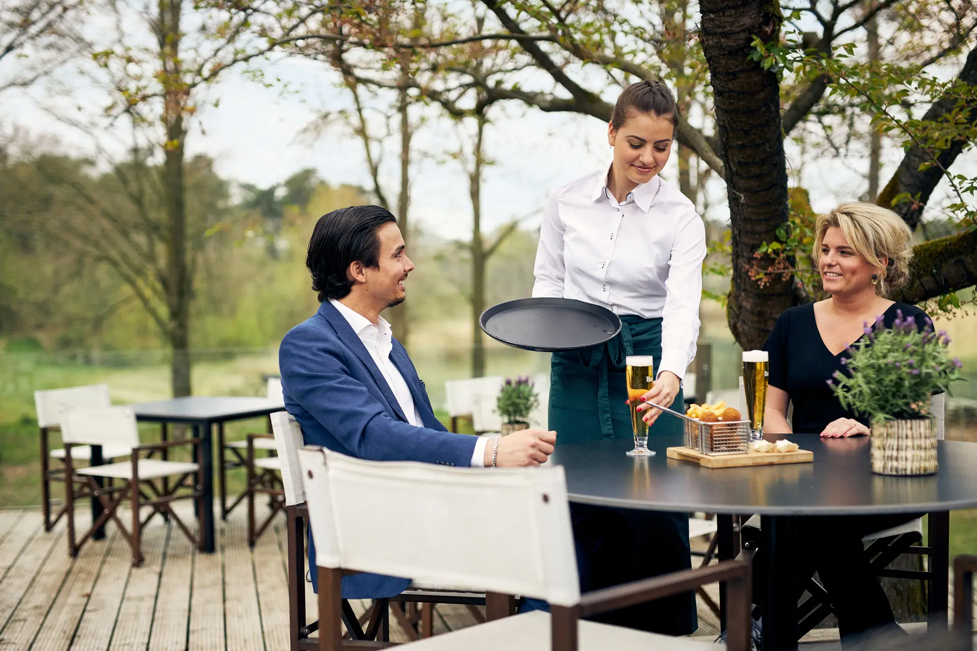 Serveerster zet een glas wijn neer buiten op een terras met een man en een vrouw