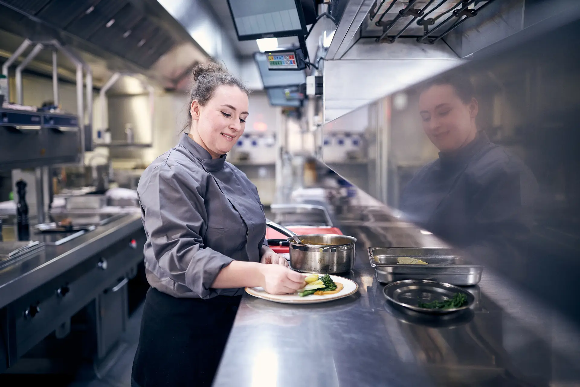 Vrouwelijke kok serveert eten uit in een industriële keuken